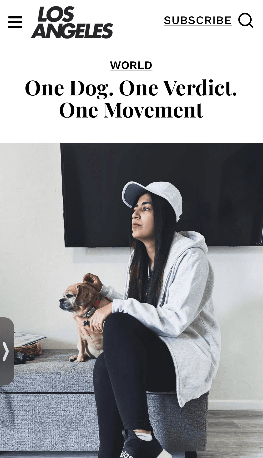 Woman in white cap and grey hoodie sits on a bench beside her small dog.