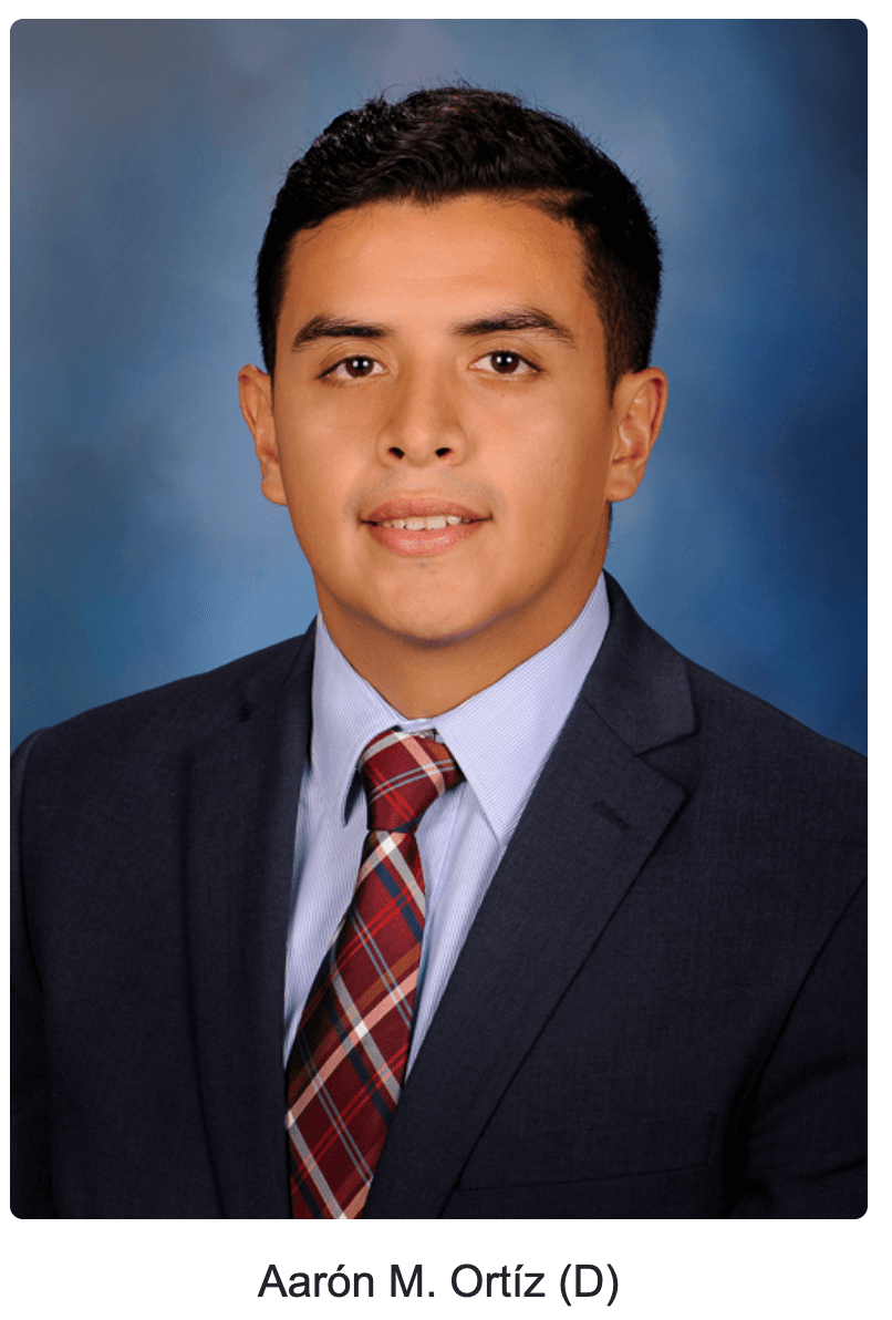 Aarón M. Ortíz wearing a navy suit, light blue shirt, and red plaid tie.